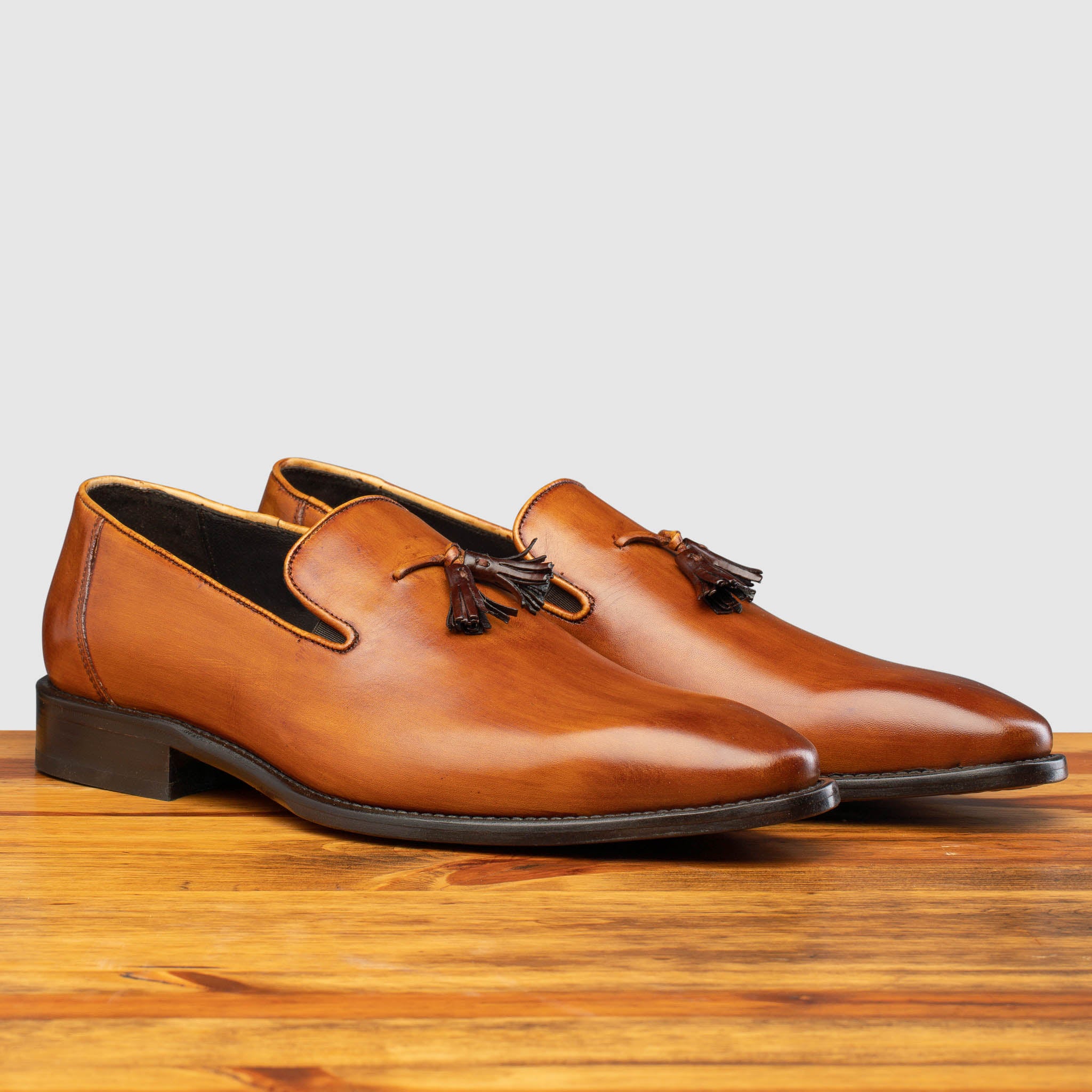 Pair of Z993 Calzoleria Toscana Dark Caramel David Tassel Slip-On on top of a wooden table